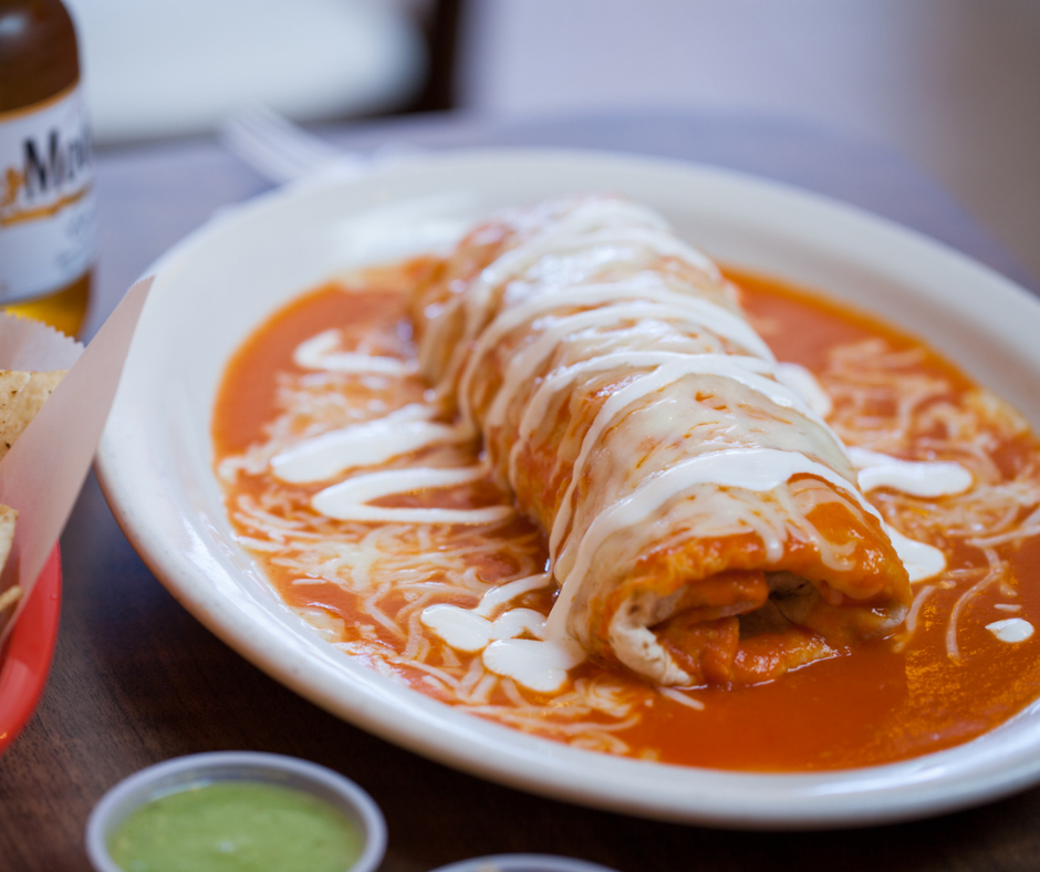 Wet burrito on a plate smothered in red sauce, cheese and sour cream.