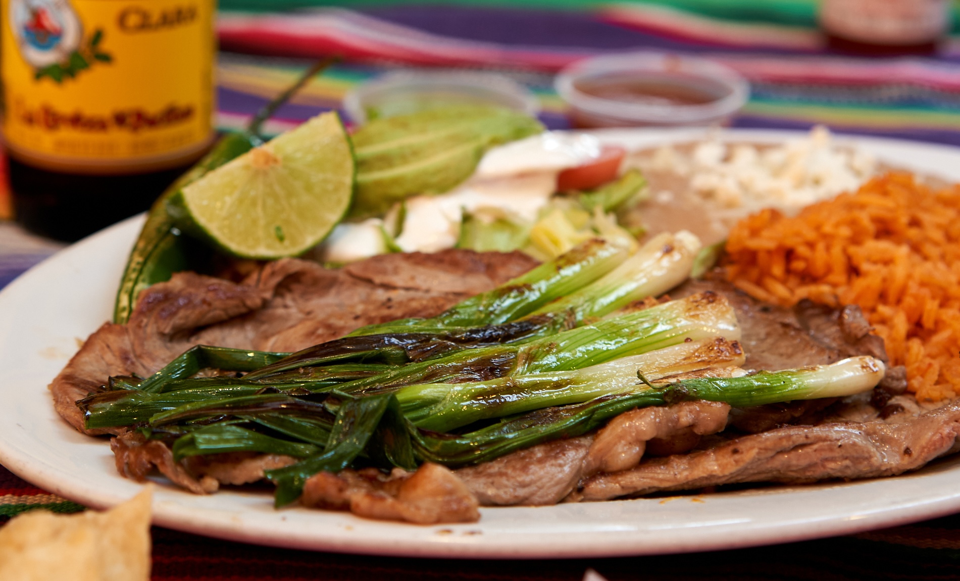 Carne asada plate with grilled spring onions, rice, beans and lime.