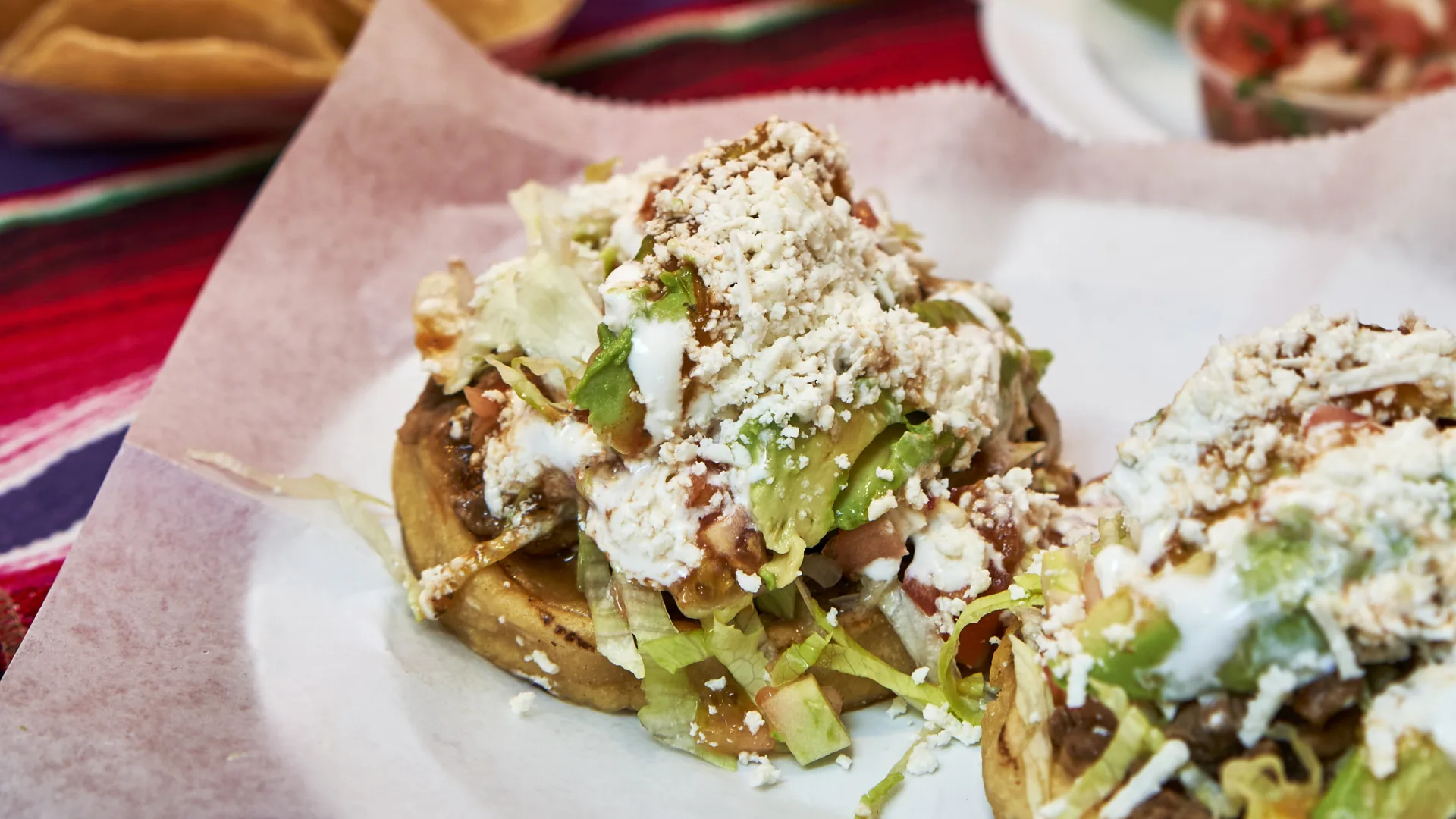 Sopes with meat, lettuce, sour cream, avocado and fresh cheese on wax paper.