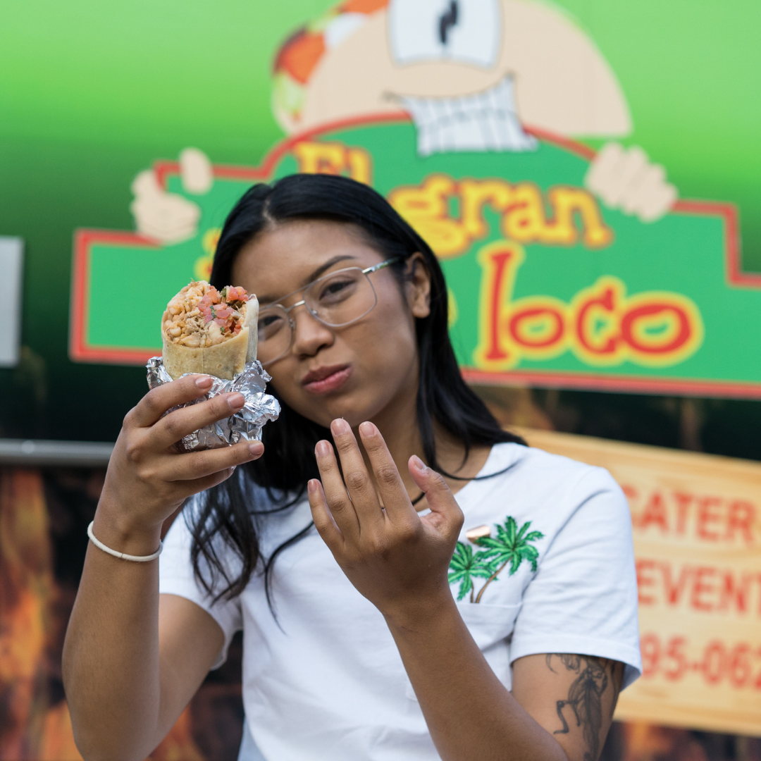 Customer holding up a foil-wrapped burrito in front of the taco truck.